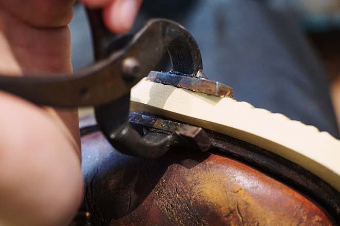 口金と呼ばれる工具を使用してコバ（側面）を貼り合わせるアイリッシュセッターの靴修理の作業